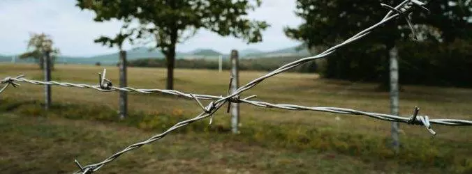 Fil de fer barbelé en croix, symbolisant le blocage ou la fermeture, devant un horizon naturel.