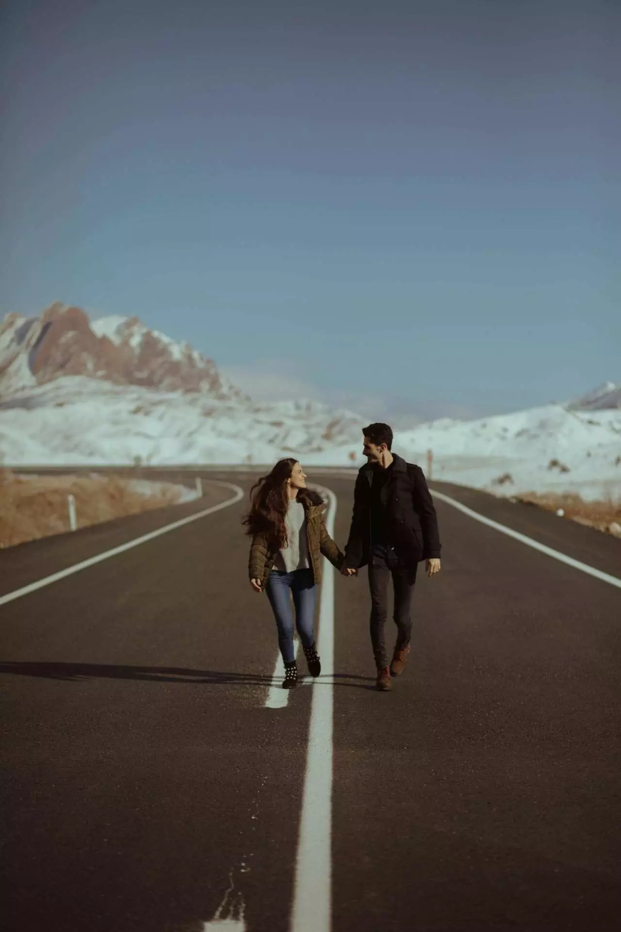 psychologue-yverdon-couple-4 Un couple marchant main dans la main sur une route avec une ligne blanche centrale, symbolisant le lien et les limites nécessaires dans une relation de couple.